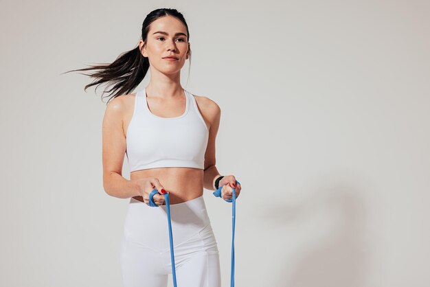 Atleta feminina confiante em roupas esportivas brancas se exercitando com faixa de resistência