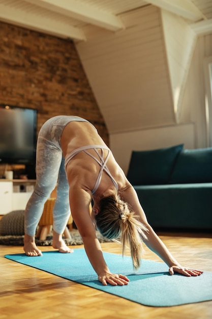 Atleta feminina em posição de cão virado para baixo praticando Yoga em casa