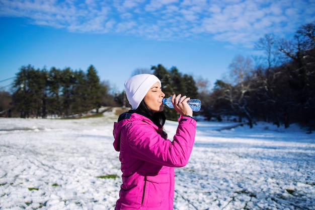 Atleta feminina em roupas de inverno, bebendo água antes de treinar na neve.