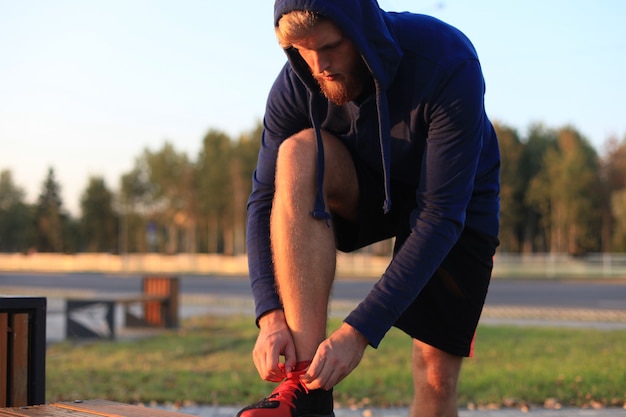 Atleta en forma. Corredor de hombre adulto guapo atar cordones de los zapatos al atardecer o al amanecer.