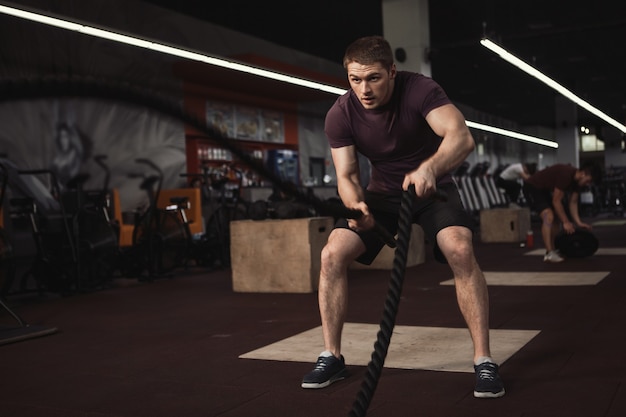 Atleta en forma cruzada trabajando con cuerdas de batalla en el gimnasio