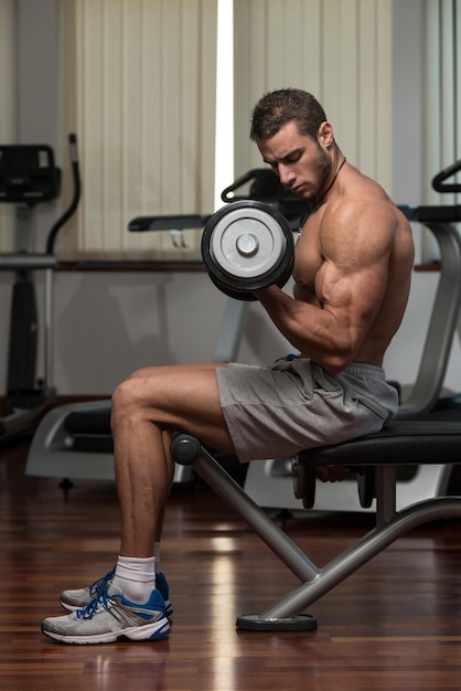 Atleta en forma trabajando bíceps rizos de concentración con mancuernas