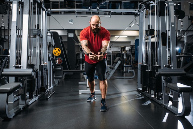 Atleta fuerte en ropa deportiva, entrenamiento en máquina de ejercicio en el gimnasio.