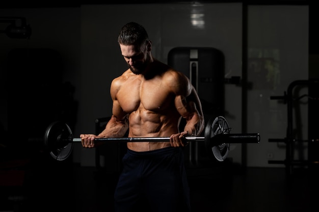 atleta en el gimnasio realizando curl de bíceps con una barra