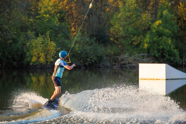 Un atleta hace un truco en el agua Un ciclista salta sobre una tabla de wakeboard contra el fondo de un bosque verde Atardecer en el lago