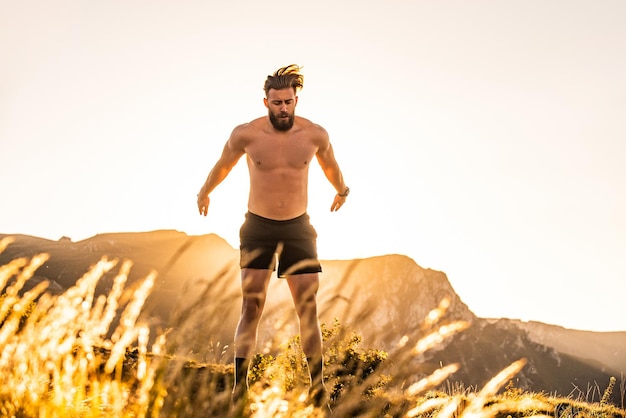 Un atleta haciendo entrenamiento de acondicionamiento en la cima de una montaña temprano en la mañana con el amanecer de fondo.