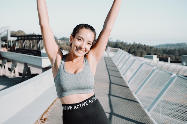 Atleta hermosa chica, piel bronceada africana. Feliz celebración después del entrenamiento urbano. Agitando los brazos y sonriendo a la cámara. Ejercicio seguro al aire libre. Polainas de ropa y top. Copie la imagen del espacio. belleza