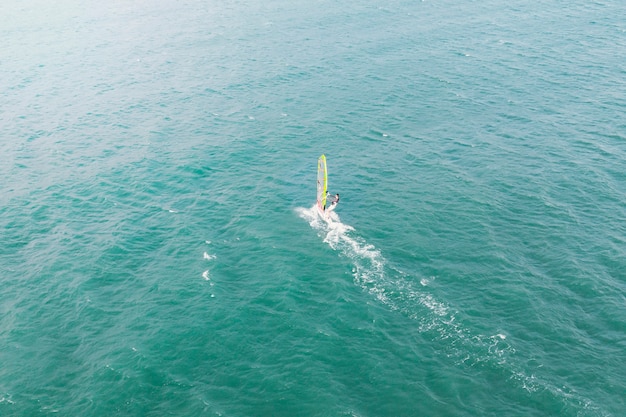 Atleta hombre extremo nada en el windsurf en la ola del mar contra el mar azul y el horizonte. Deportes acuáticos extremos. movimiento de la vela roja sobre el agua. diversión de verano en el mar.