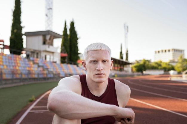 Atleta hombre pose de relajación sentado en la pista de atletismo