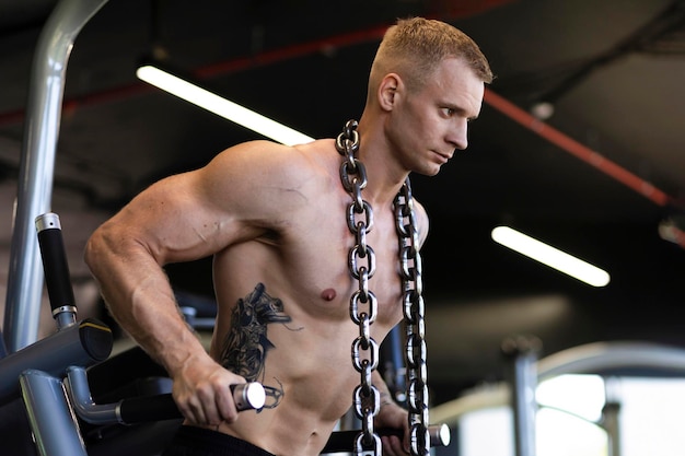Foto atleta homem fisiculturista malhando academia de treinamento com corrente no pescoço ganhando peso bombeando