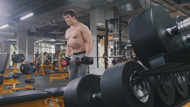 Atleta homem levantando halteres sem camisa na academia, close-up