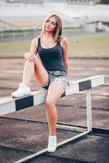 Atleta iniciante senta-se em um obstáculo de tênis branco em um estádio com um sorriso no rosto