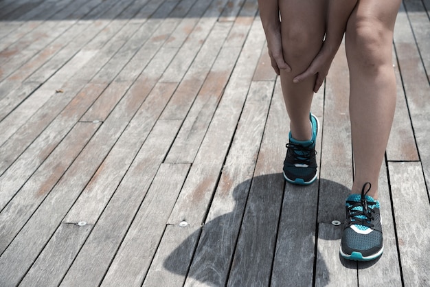 Atleta irreconhecível com sapatos azuis tocando a perna tensa enquanto está de pé em uma superfície de madeira ao ar livre