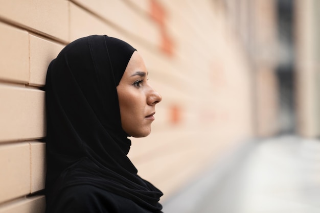 Atleta islâmica jovem séria em hijab se inclina na parede de tijolos pensa e descansa depois de correr