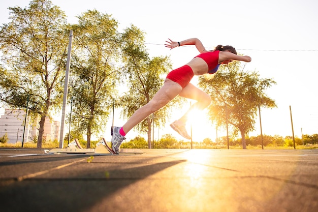 Foto atleta jovem com um braço amputado e queimaduras no corpo corre ao redor do campo esportivo ela treina correndo do bloco de partida ao ar livre ao pôr do sol
