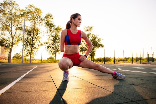 Atleta jovem com um braço amputado e queimaduras no corpo se alonga no campo esportivo Treinamento ao ar livre ao pôr do sol