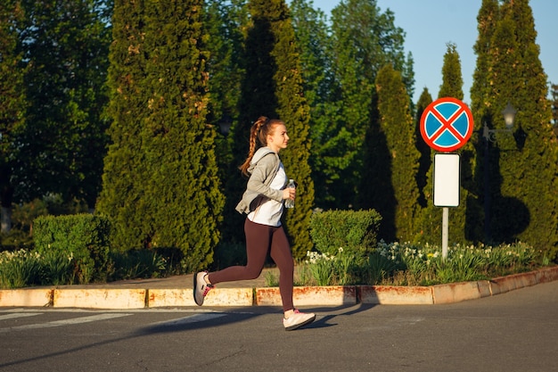 Atleta jovem corredor feminino está correndo na rua da cidade sob o sol