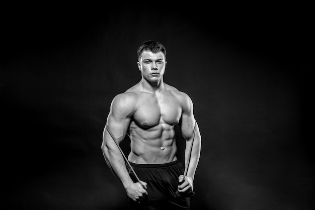 Atleta jovem sexy, posando em um fundo preto no estúdio. Fitness, musculação, preto e branco