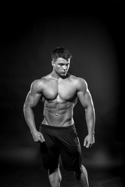 Atleta jovem sexy, posando em um fundo preto no estúdio. Fitness, musculação, preto e branco