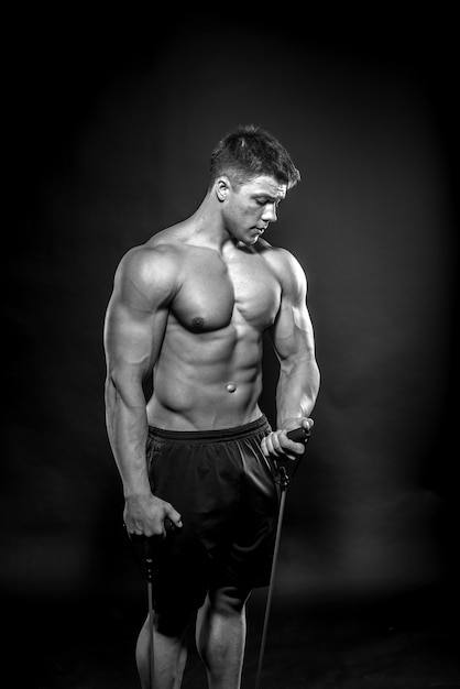 Atleta jovem sexy, posando em um fundo preto no estúdio. Fitness, musculação, preto e branco.