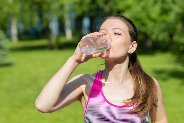Atleta joven bebiendo agua en el entrenamiento al aire libre. niña sedienta haciendo deporte en un caluroso día de verano