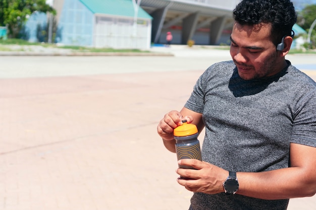 Atleta joven cansado con botella de agua en el parque