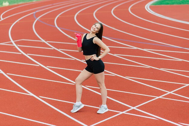 Atleta joven, hermosa chica en ropa deportiva está entrenando y corriendo, estirando en el estadio