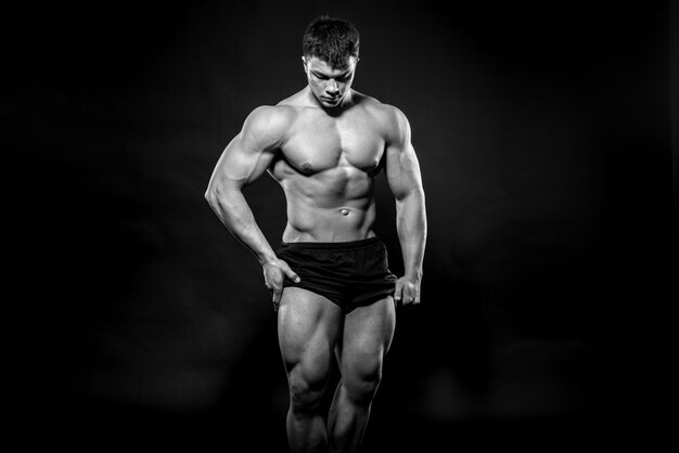 Atleta joven sexy posando sobre un fondo negro en el estudio. Fitness, culturismo, blanco y negro.