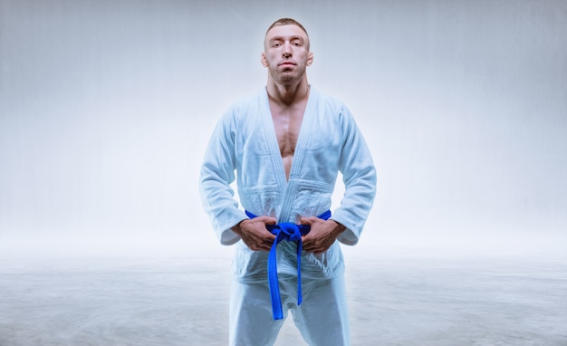 Atleta en un kimono con un cinturón azul se encuentra sobre un fondo claro. El concepto de karate y judo. Técnica mixta