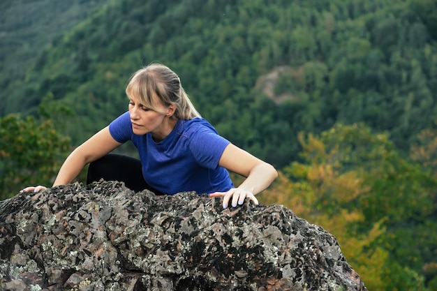 Atleta loira enquanto escala uma montanha alta, superando obstáculos no caminho