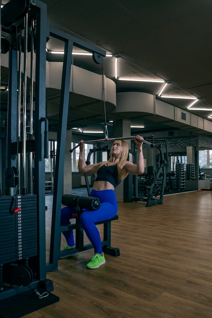 Atleta loira no ginásio fazendo exercício de impulso vertical para os músculos das costas Pulldown