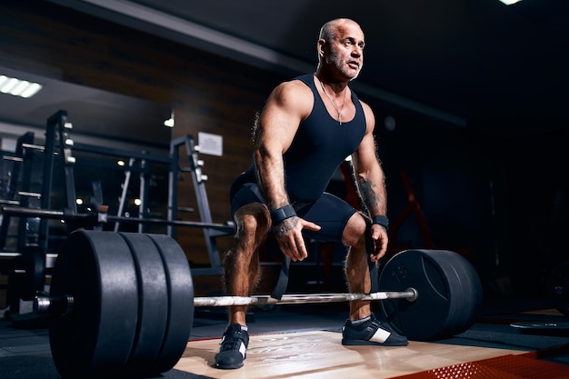 Atleta mais velho se preparando para fazer levantamento terra com barra durante o treinamento cruzado em uma academia