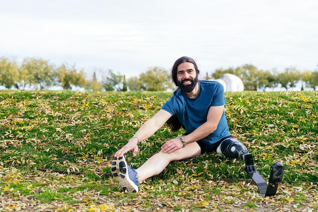 Atleta masculino alegre com uma perna protética de fibra de carbono sentado ao ar livre, alongando-se antes de uma corrida