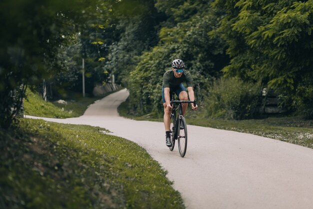 Atleta masculino andando de bicicleta preta em meio ao parque verde da cidade