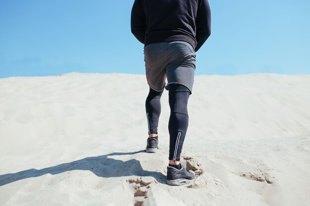 Atleta Masculino se ejecuta en una montaña de arena piernas closeup