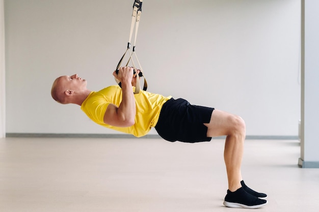 Un atleta masculino enfocado realizando un ejercicio en bucles funcionales en el gimnasio.