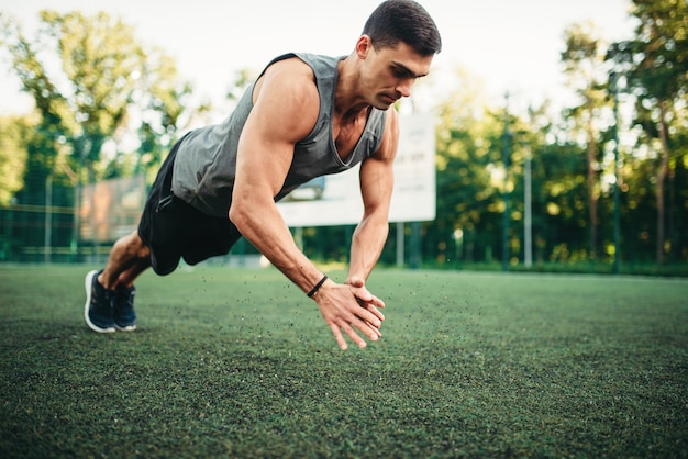 Atleta masculino en entrenamiento, ejercicio de flexiones en acción, entrenamiento físico. Deportista en el parque