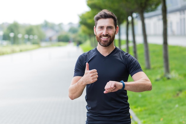 Atleta masculino exitoso que hace fitness por la mañana, descansando y sonriendo se regocija con el resultado del entrenamiento en el parque