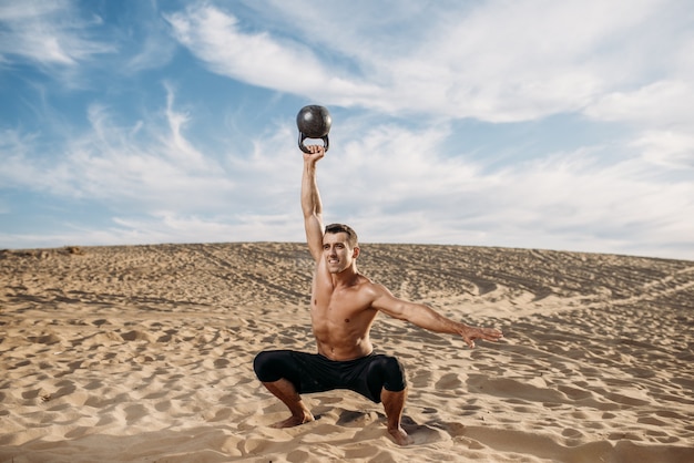 Atleta masculino fazendo exercícios com pesos no deserto em dia ensolarado. Forte motivação no esporte, treinamento de força ao ar livre