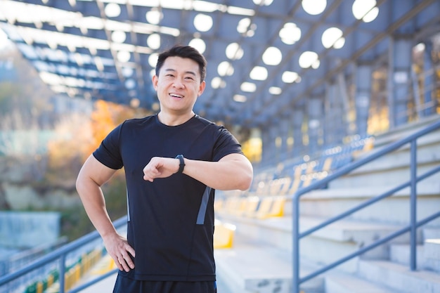 Atleta masculino feliz e bem-sucedido olha para a câmera e sorri asiático feliz com o resultado de seu treinamento perto do estádio do lado de fora pela manhã