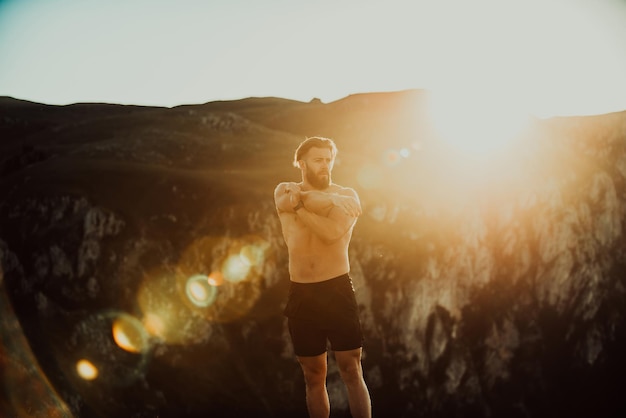 Atleta masculino haciendo ejercicio de estiramiento de brazos en la cima de una montaña.