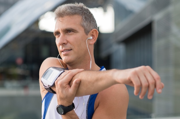 Atleta masculino maduro se alongando e ouvindo música ao ar livre