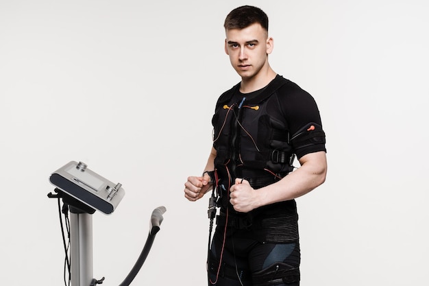 Atleta masculino musculoso em traje de EMS em treinamento esportivo de fundo branco em traje de estimulação muscular elétrica
