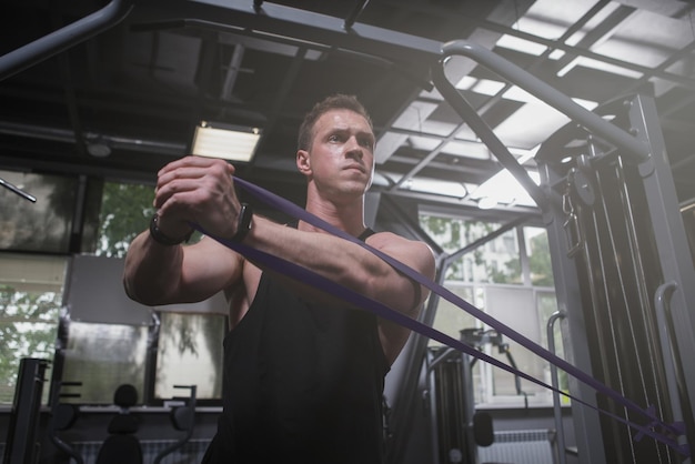 Atleta masculino musculoso treinando com elástico de resistência no estúdio de esportes