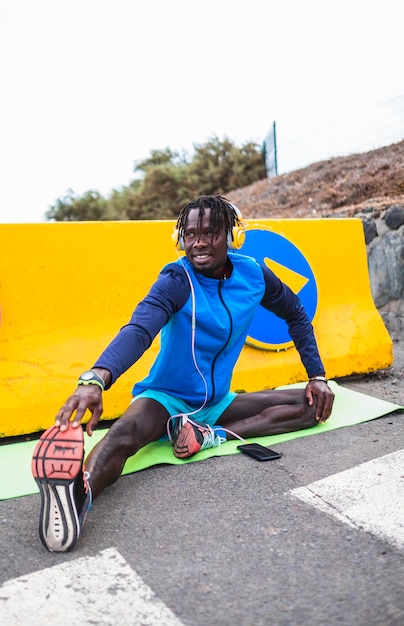 atleta masculino negro vestido con ropa deportiva, estirándose antes de comenzar a hacer ejercicio.