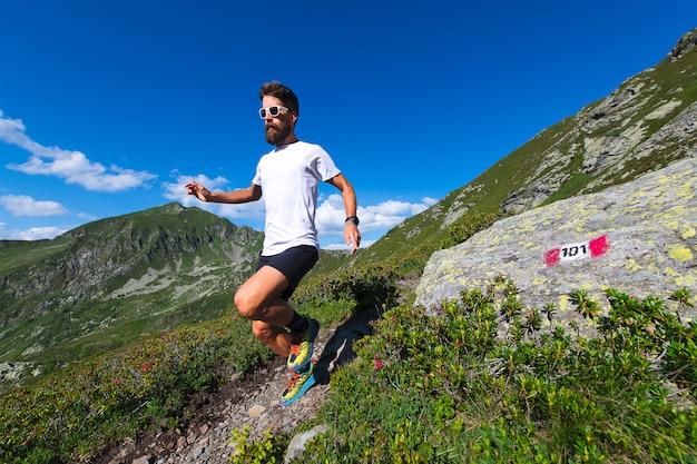 Atleta masculino praticando montanha correndo em uma trilha marcada pelos alpes oróbicos