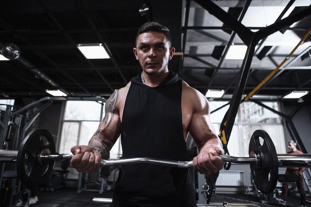 Atleta masculino rasgado centrado que ejercita con barra en el gimnasio