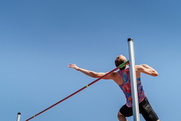 Atleta masculino de salto de altura en el fondo del cielo azul