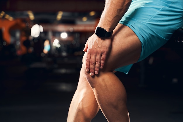 Un atleta masculino se siente adolorido y se toca la rodilla en un gimnasio oscuro