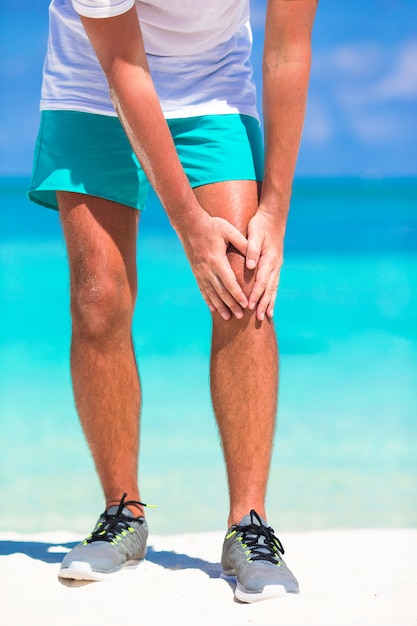 Atleta masculino, sofrendo de dor na perna durante o exercício na praia branca